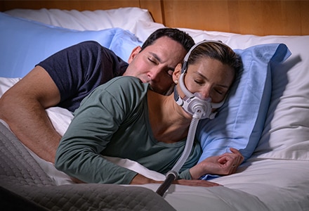 Eine Frau, die mit der ResMed AirFit F40 CPAP-Maske friedlich auf der Seite schläft, während ihr Partner sich hinter sie kuschelt.