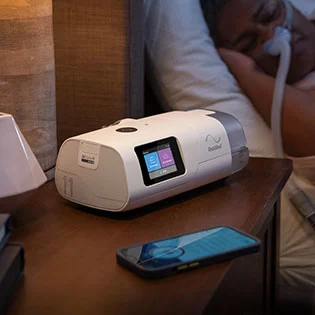 Das AirCurve 11 ASV PaceWave-Gerät wird auf einem Nachttisch gezeigt, während sein Benutzer schläft, mit einem Mobiltelefon daneben.